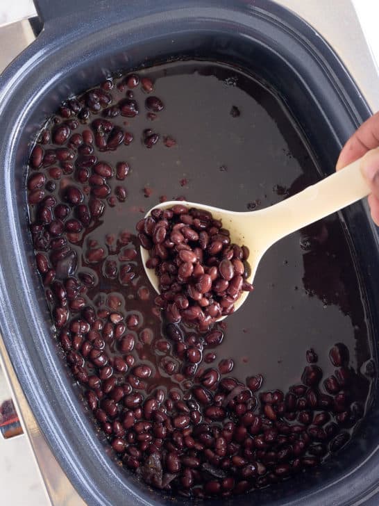 A scoop of black beans being lifted out of the slow cooker.