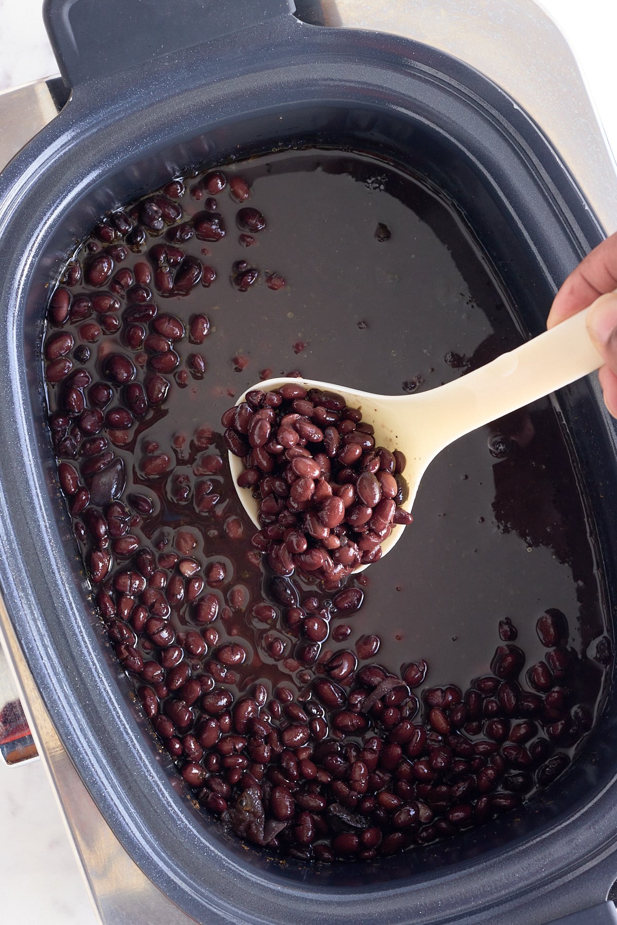 A scoop of black beans being lifted out of the slow cooker.