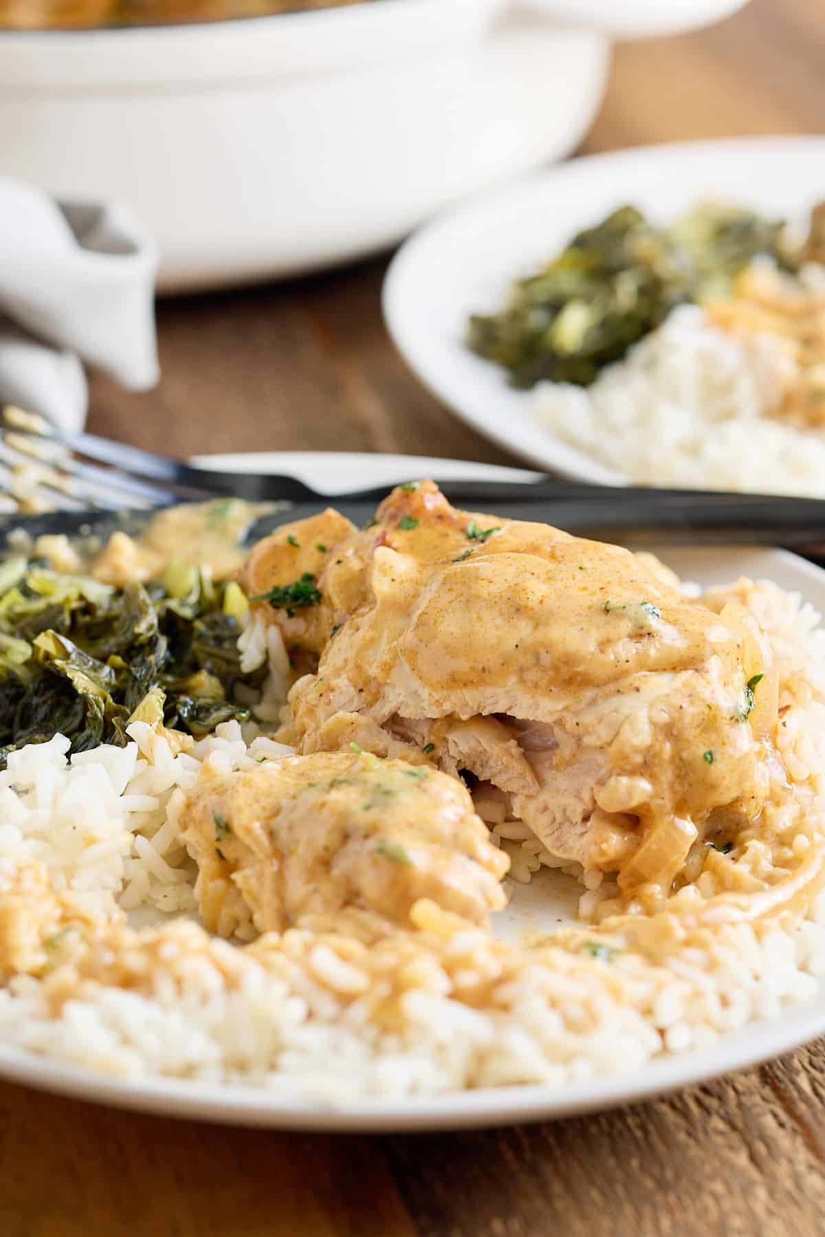 Close up image of white plate with smothered chicken served with steamed white rice and sauteed greens