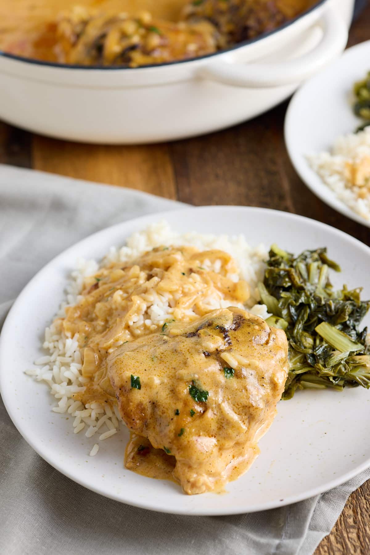 White plate with smothered chicken served with steamed white rice and sauteed greens