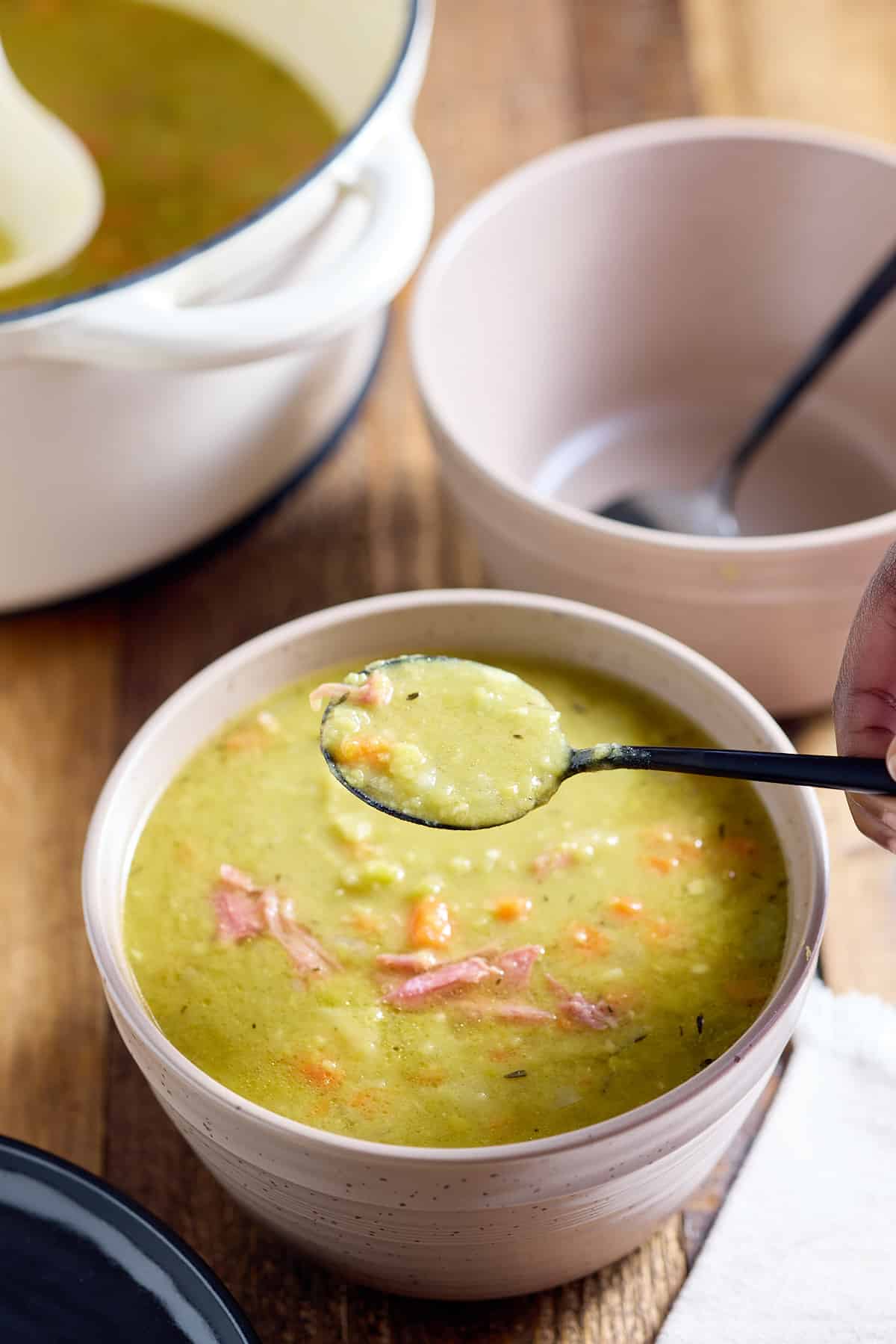A bowl full of warm split pea soup with ham and a spoon.
