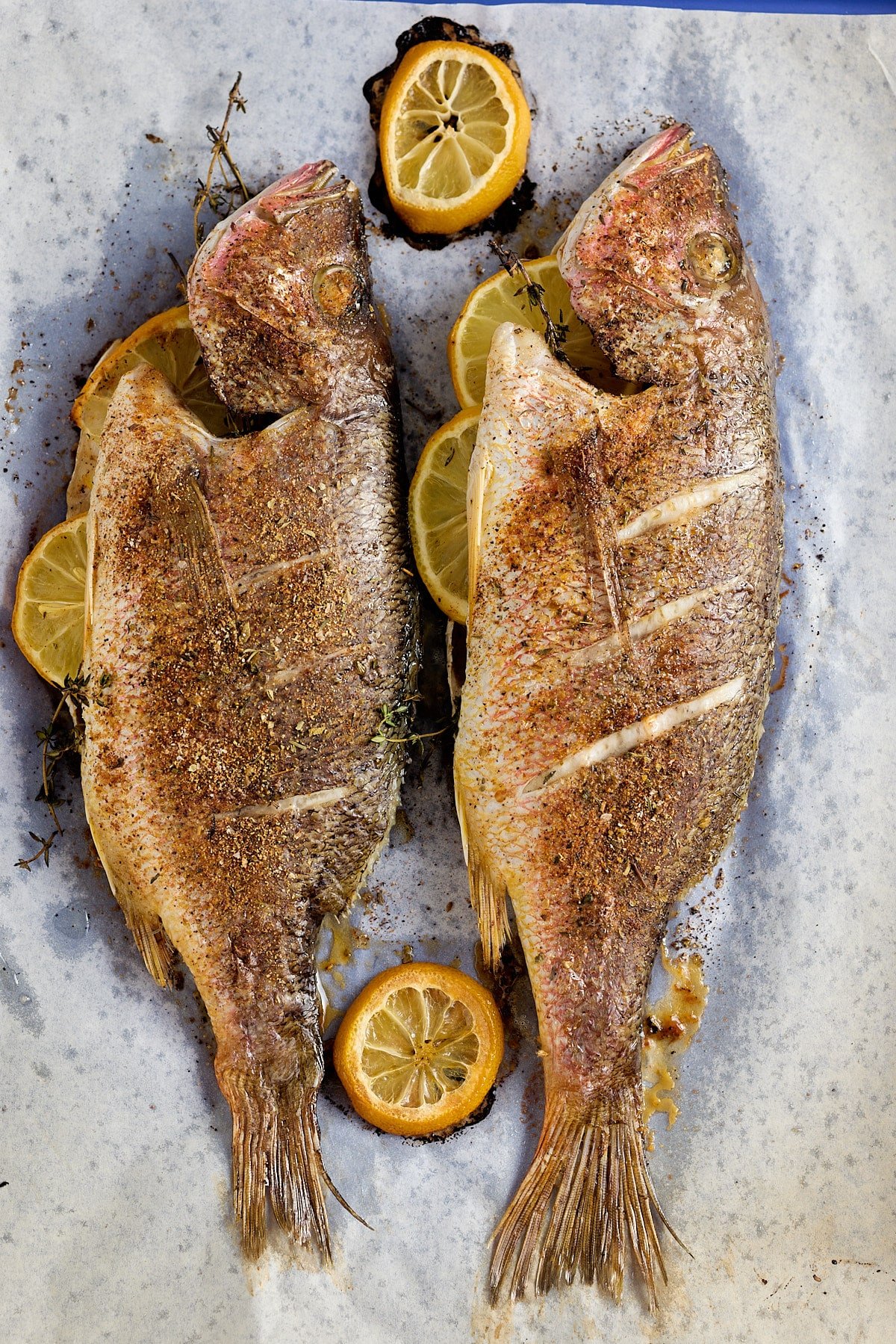 cooked whole fish stuffed with fresh thyme and lemon slices set on parchment paper