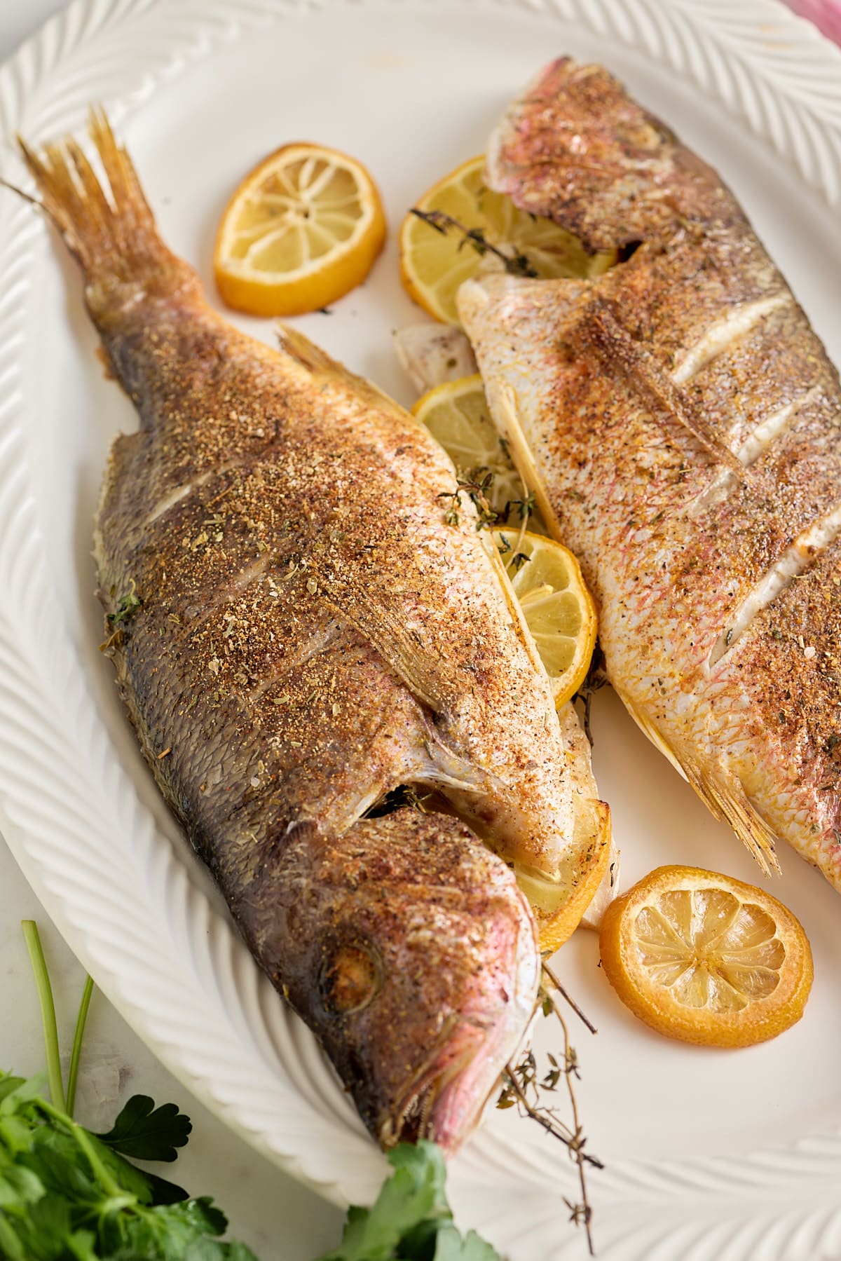 white serving platter with 2 cooked whole fish stuffed with fresh thyme and lemon slices