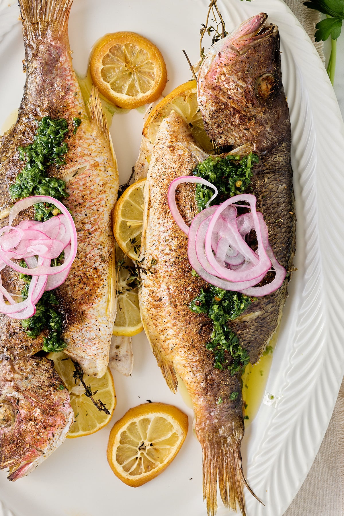 close up image of white serving platter with 2 cooked whole fish stuffed with fresh thyme and lemon slices