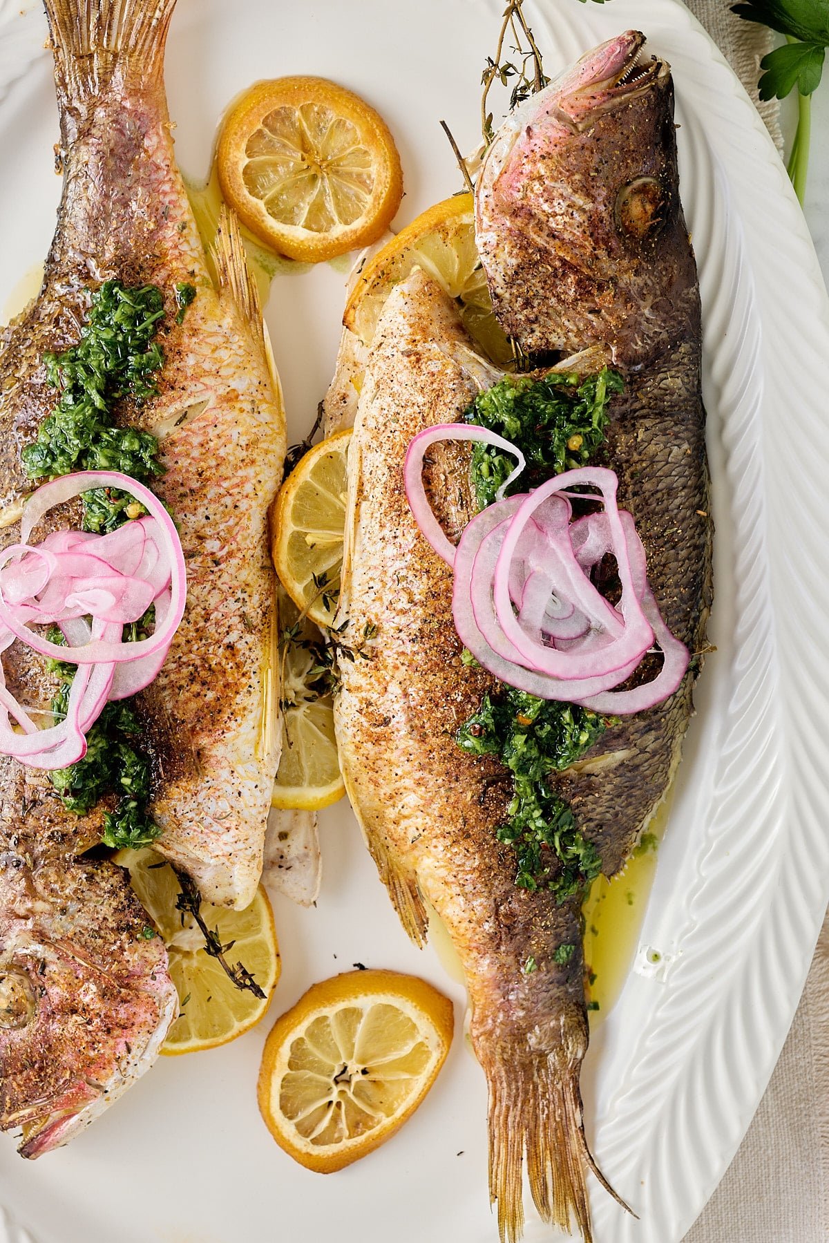 close up image of white serving platter with 2 cooked whole fish stuffed with fresh thyme and lemon slices