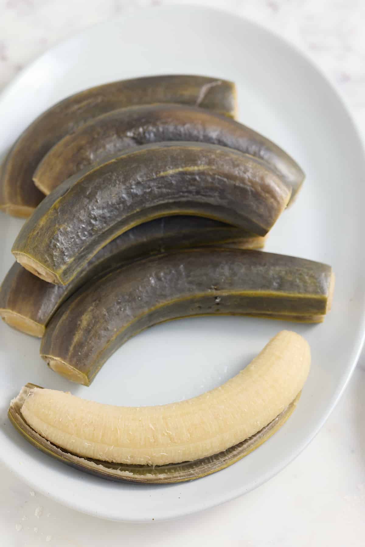 boiled green banana with one peeled on white plate
