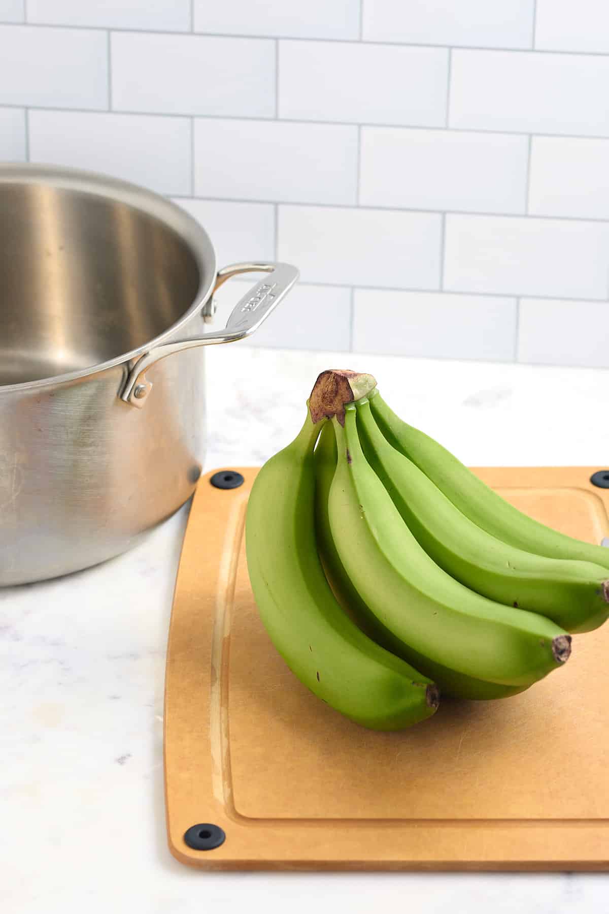 green banana on cutting board in front of large pot