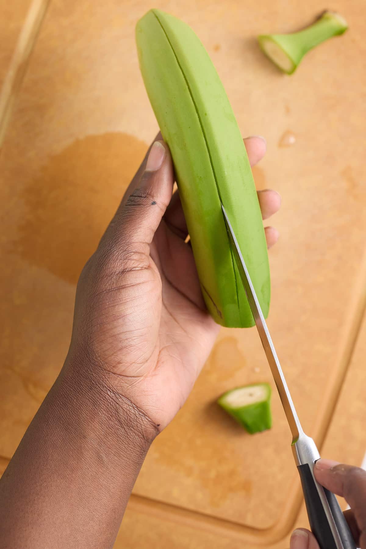 hand cutting slits down the side of a green banana