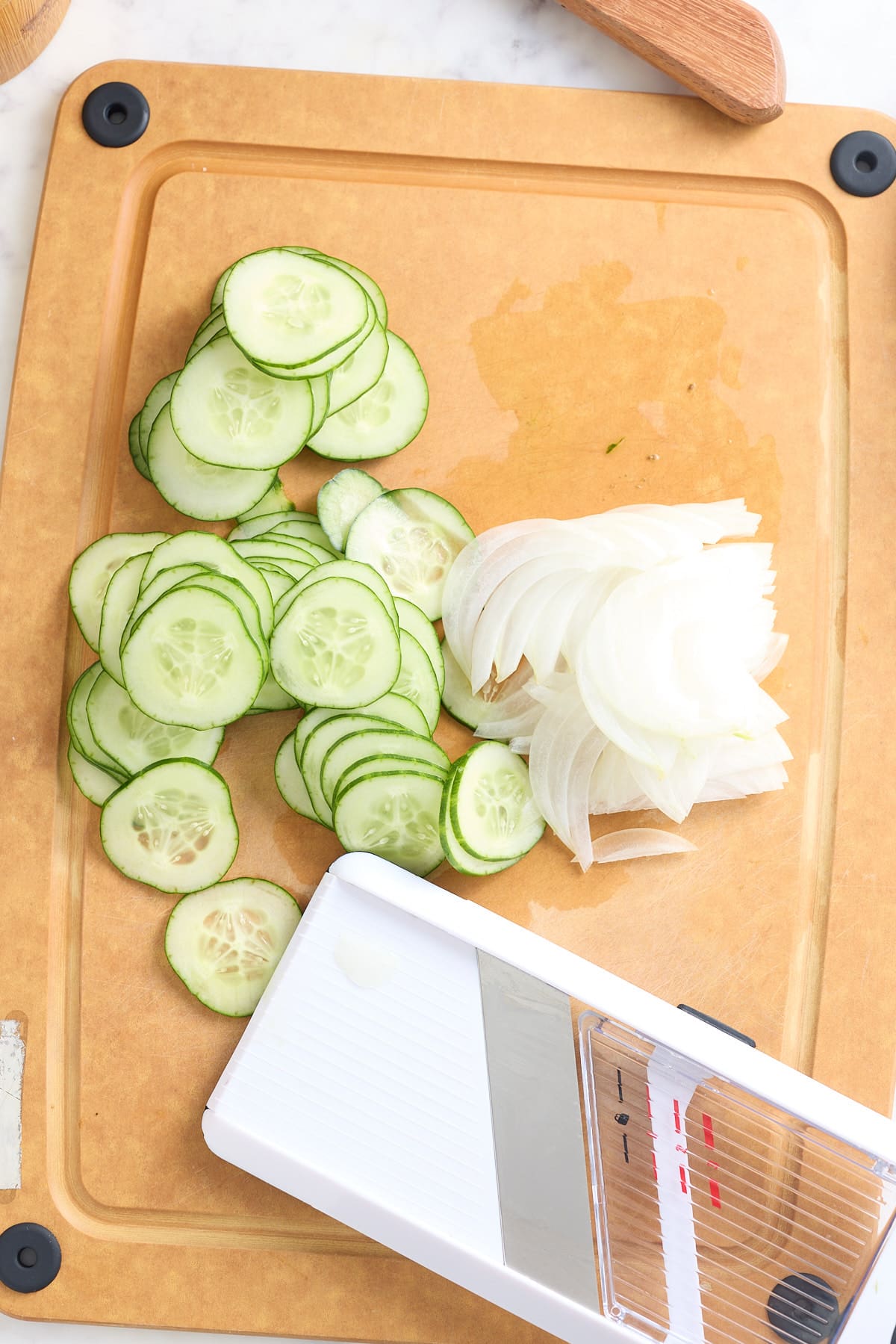 mandolin and thinly sliced cucumber and sweet onion set on a wooden board