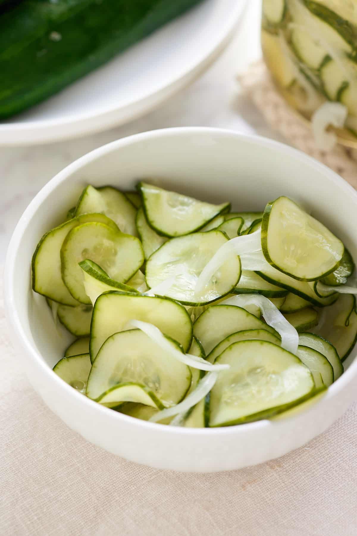 a white bowl filled with thinly sliced cucumber and sweet onion pickles
