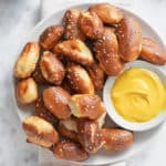 a top down image of a white bowl piled with air fried pretzel bites and a bowl of mustard dipping sauce
