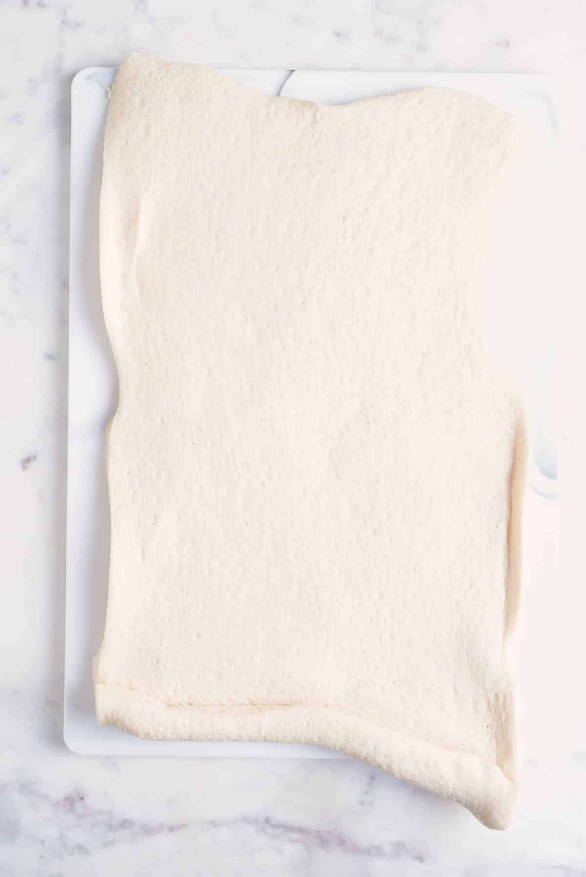 a sheet of pizza dough spread out on a board