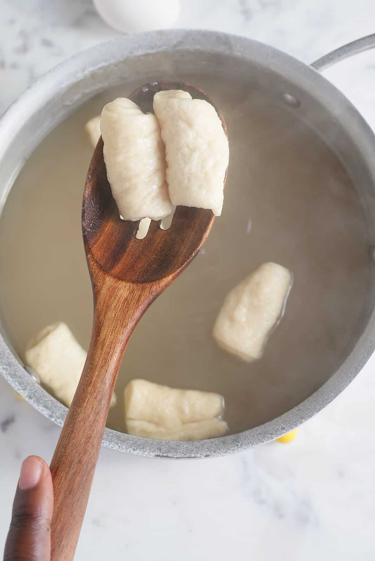a pot of water and slotted spoon with balls of cooked dough