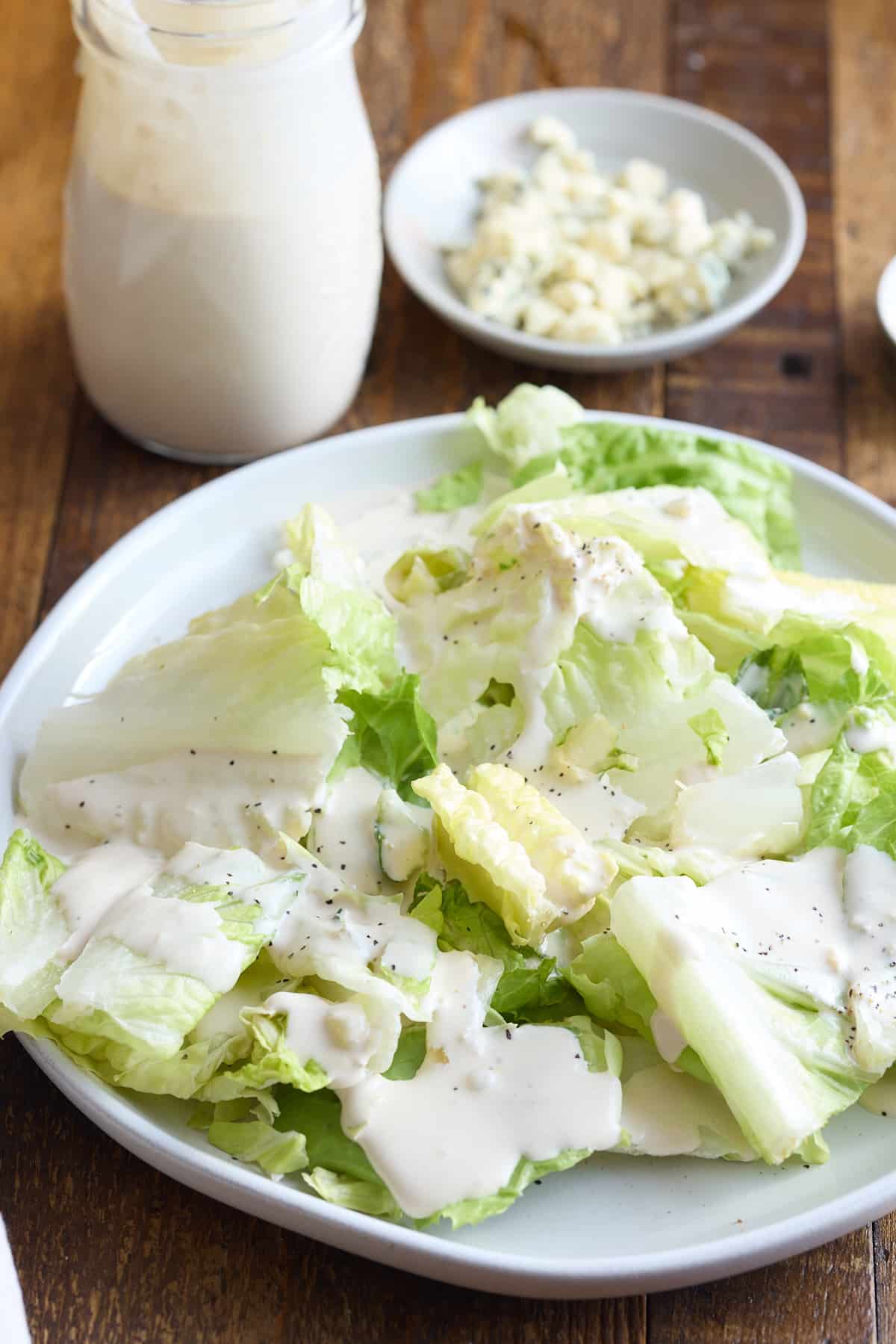 a white plate of romaine lettuce drizzled with blue cheese dressing, set on a wooden board with a jar of blue cheese dressing set alongside