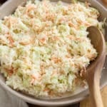 Coleslaw in a serving bowl with a wooden spoon.