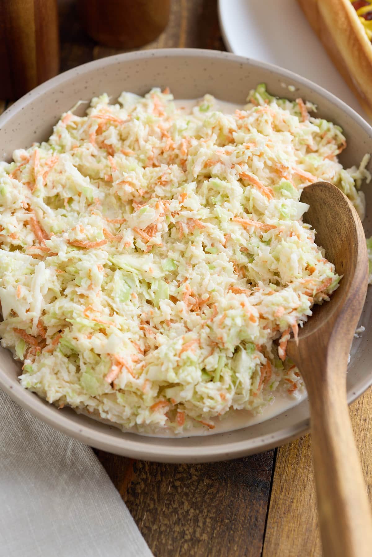 Coleslaw in a serving bowl with a wooden spoon.