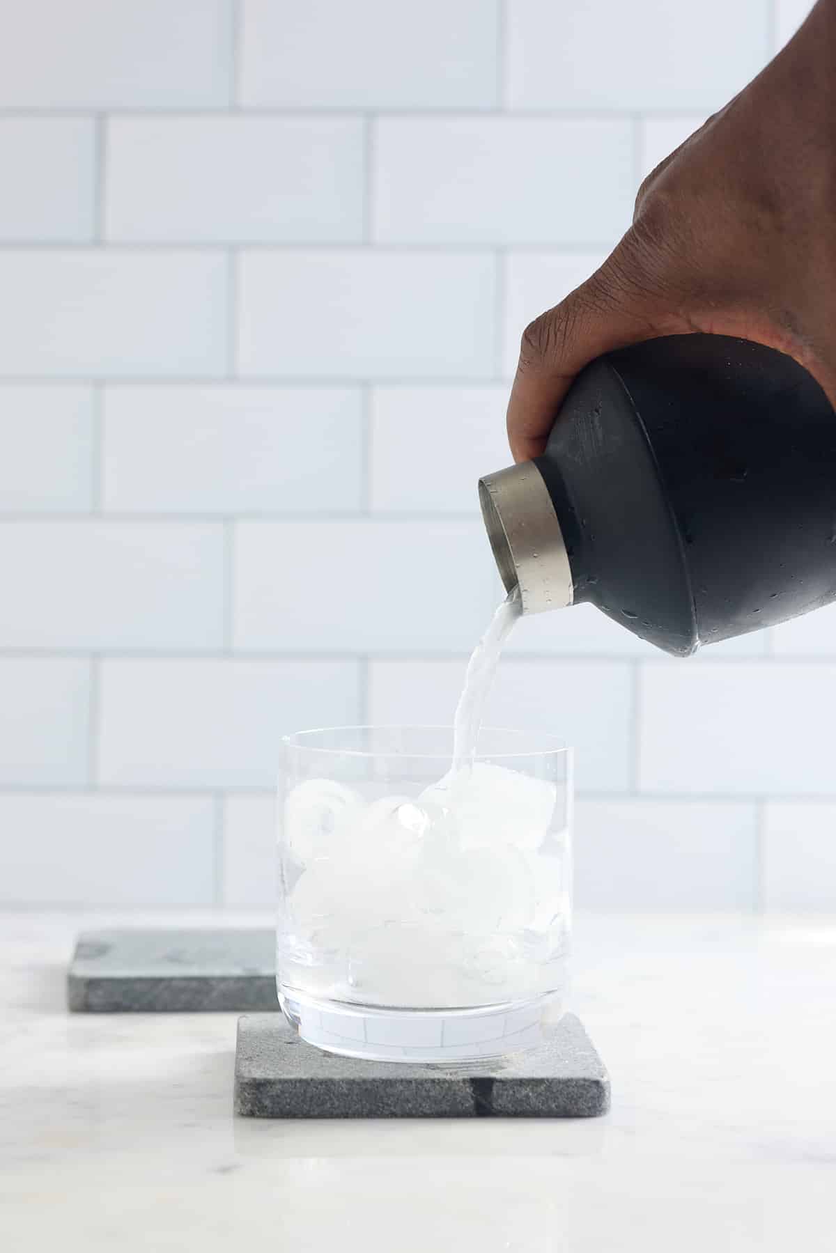 cocktail shaker pouring liquid into a glass filled with ice