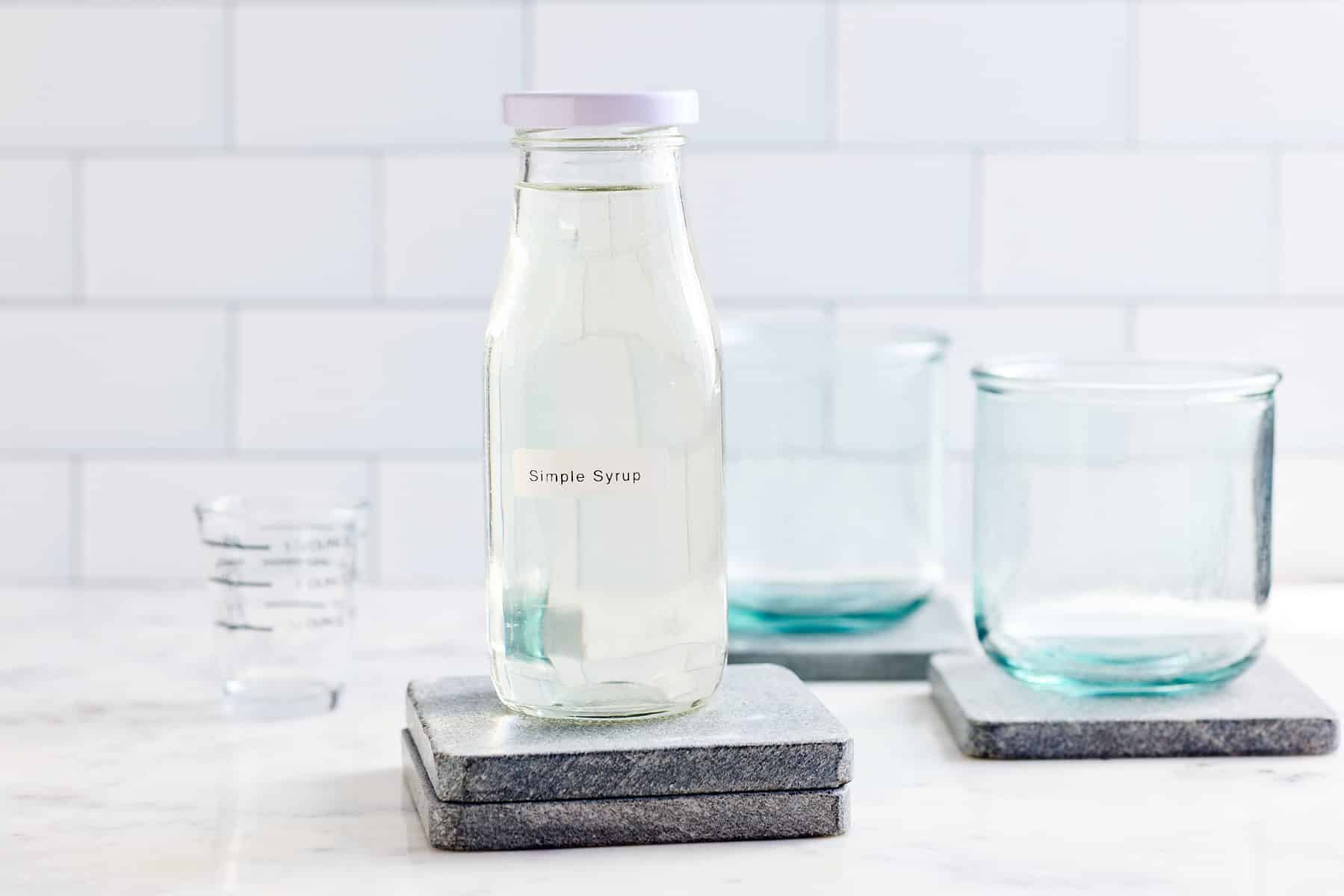 labeled glass jar filled with simple syrup and glasses set alongside