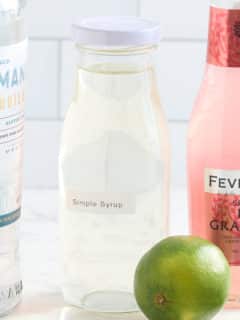 glass bottle filled with simple syrup with a bottle of tequila, grapefruit tonic and a fresh lime