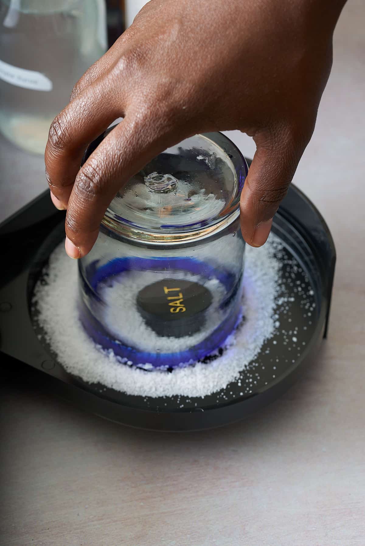 the rim of a glass being dipped into a shallow black dish of coarse salt