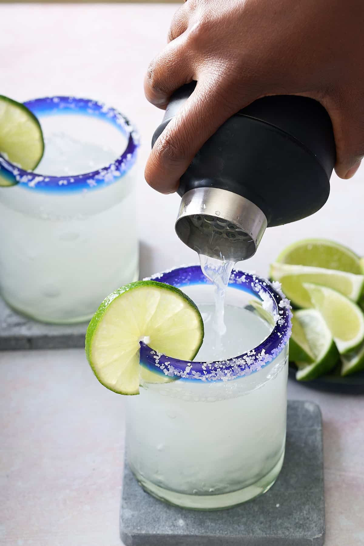 2 salt rimmed glasses, garnished with a slice of fresh lime being filled with classic margarita from a cocktail shaker