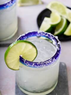 salt rimed glass garnished with a slice of fresh lime filled with classic margarita cocktail