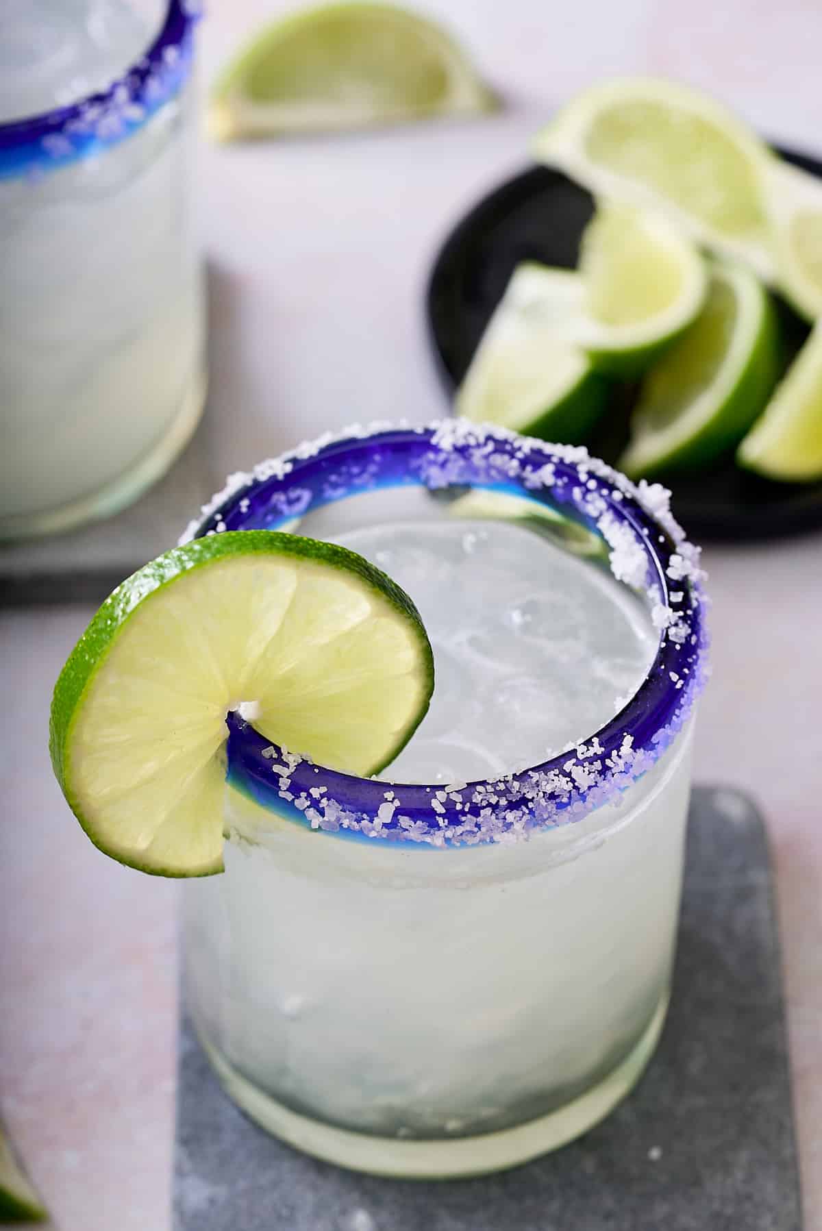 salt rimed glass garnished with a slice of fresh lime filled with classic margarita cocktail