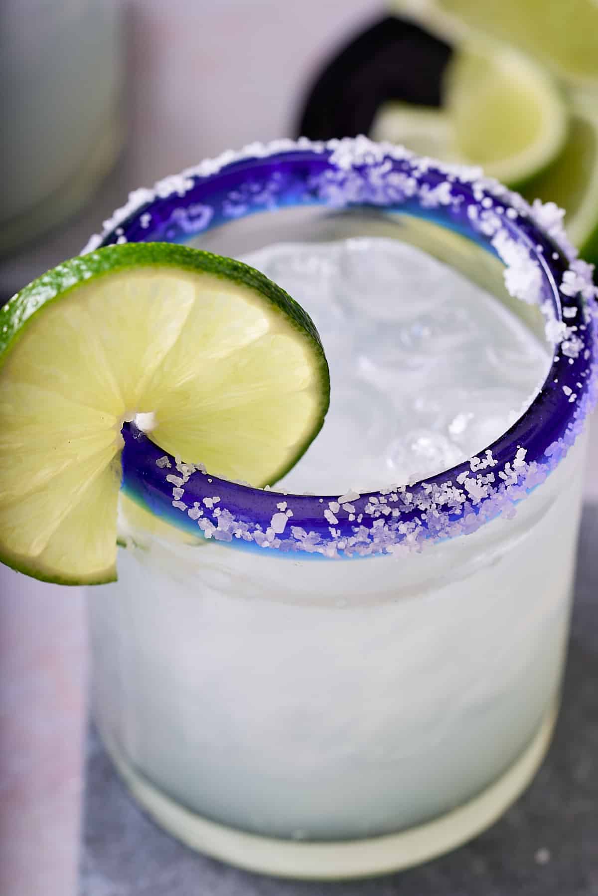 close up image of a salt rimed glass garnished with a slice of fresh lime filled with classic margarita cocktail