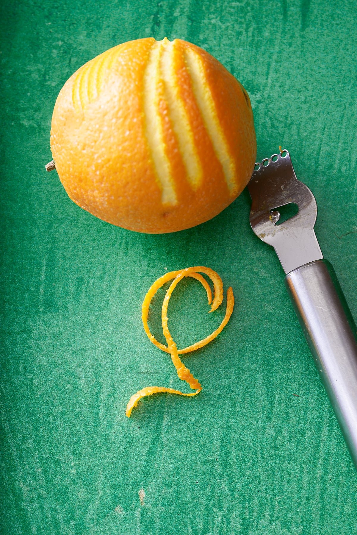 whole orange on a green board with an orange peeling and some strips of orange peel