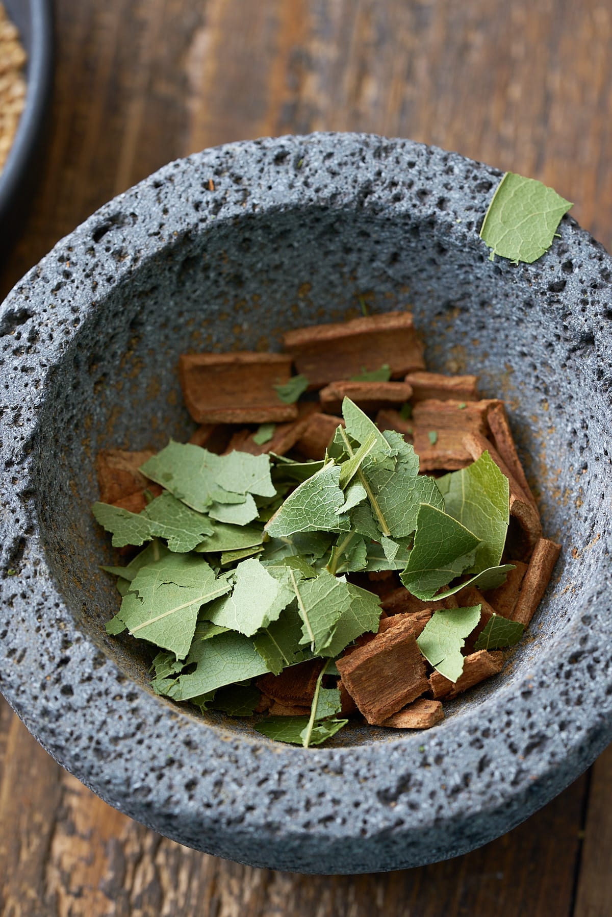 Pestle and mortar filled with whole spices, crushed cinnamon sticks and bay leaves, set on a wooden board.