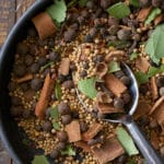 A black bowl filled with a combination of pickling spice, including dried whole spices including allspice berries, mustard seeds, black peppercorns, crushed cinnamon sticks, bay leaves and coriander seeds.