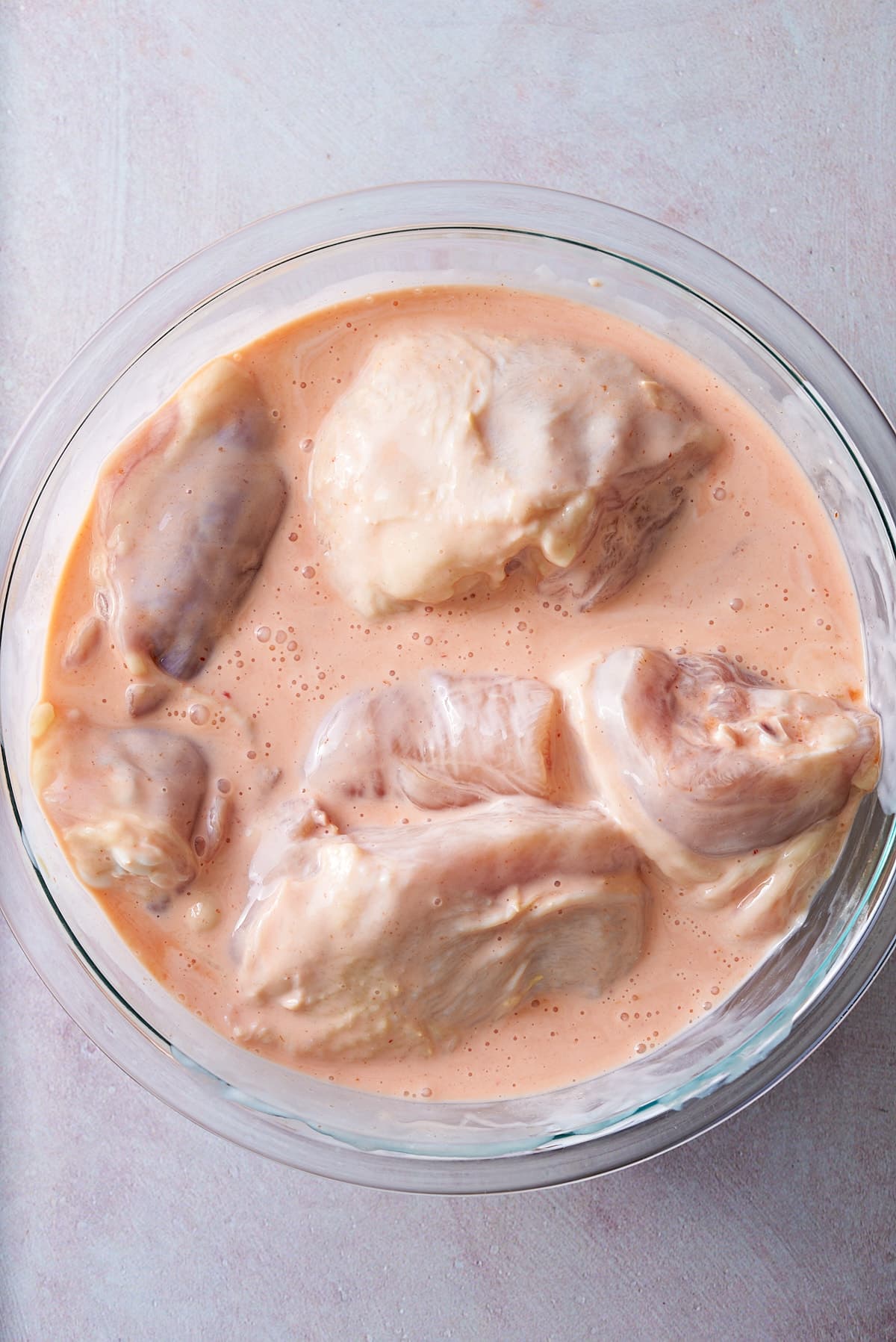 A glass bowl filled with pieces of chicken covered in a buttermilk and hot sauce brining liquid.