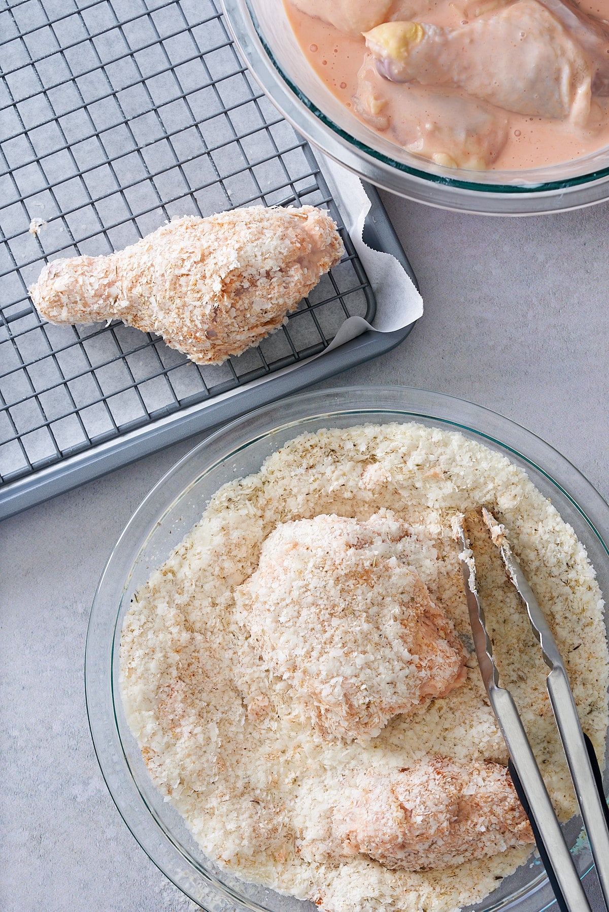 Pieces of chicken being coated in a crumb mix and a tray with a wire rack set on top with crumbed pieces of chicken on top.