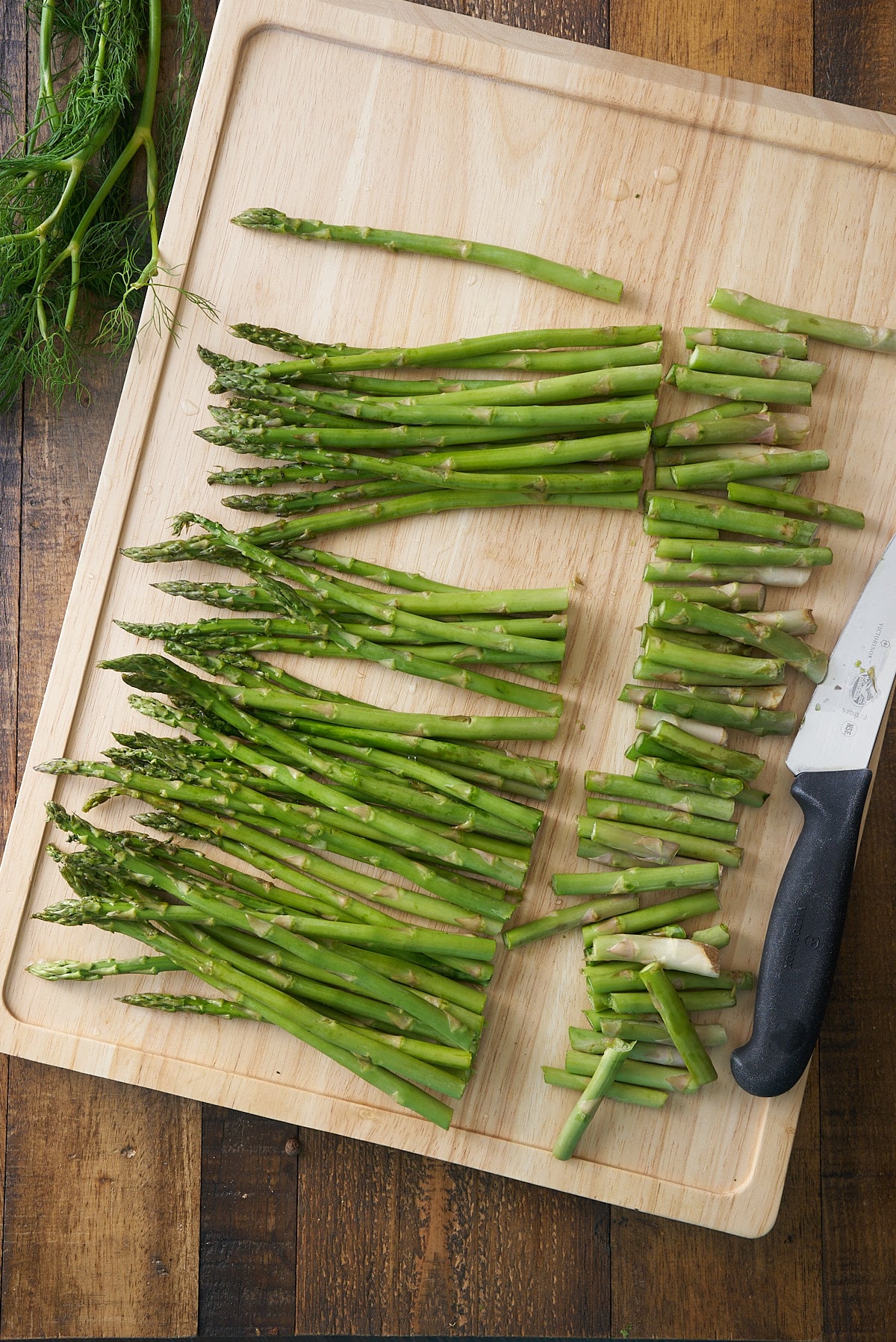 Asparagus spears set on a wooden chopping board with the woody base of the stem removed.