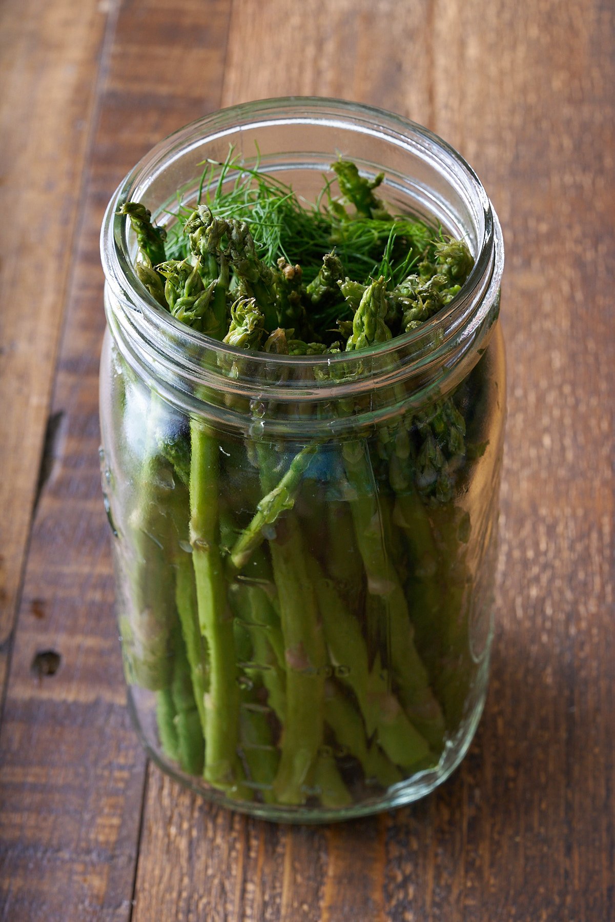 A glass mason jar filled with upright asparagus spears and fresh stems of dill.