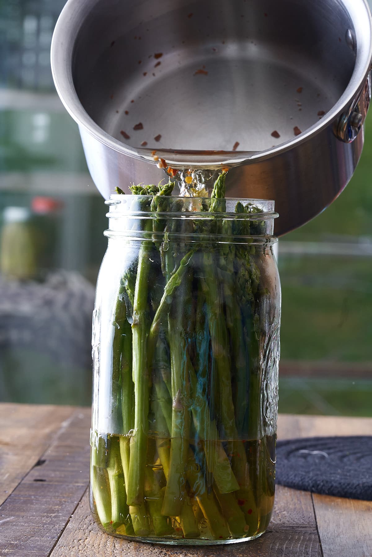 Asparagus spears set upright in a glass mason jar being topped up with pickling liquid.