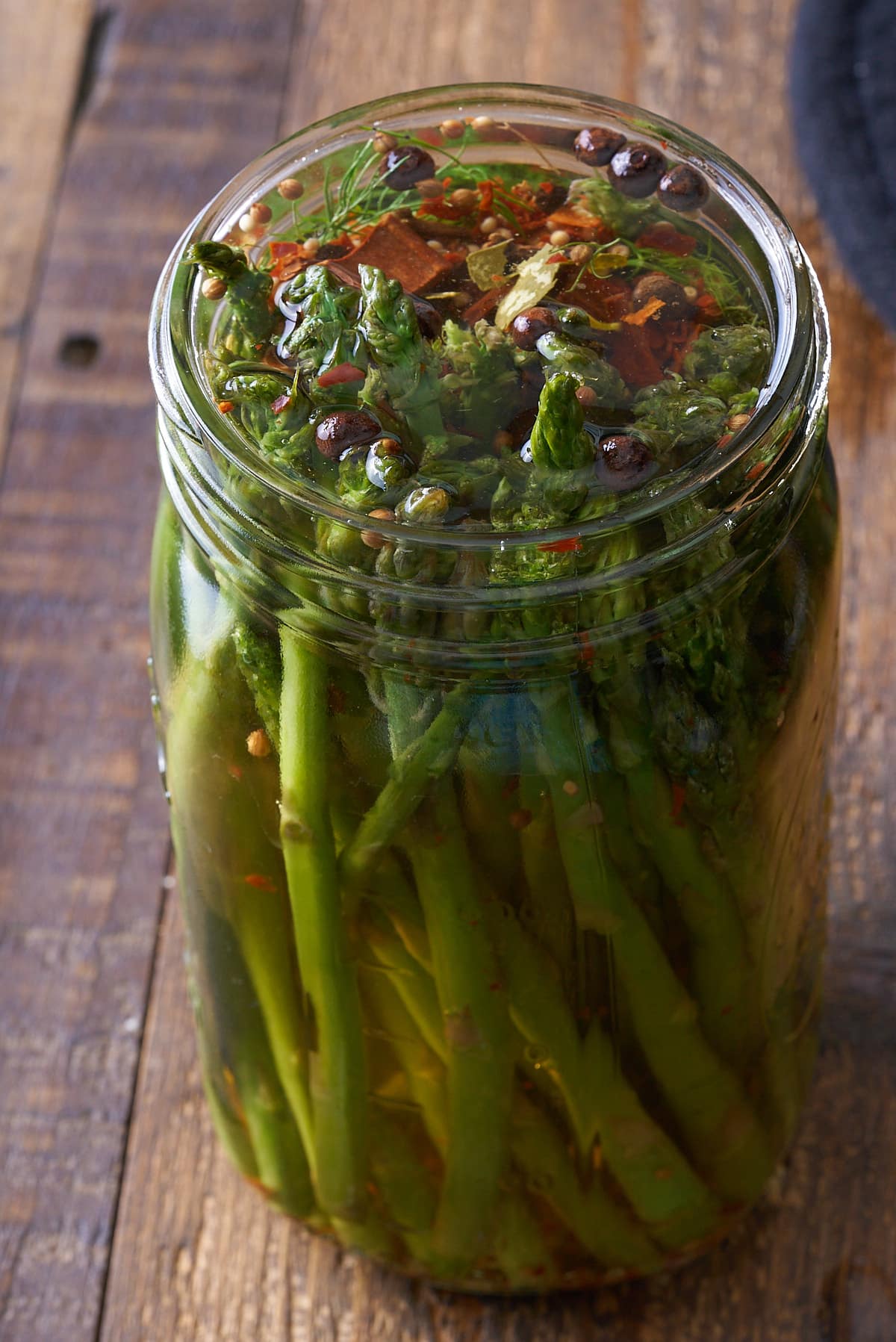 A glass mason jar filled with upright spears of asparagus topped up with pickling liquid.