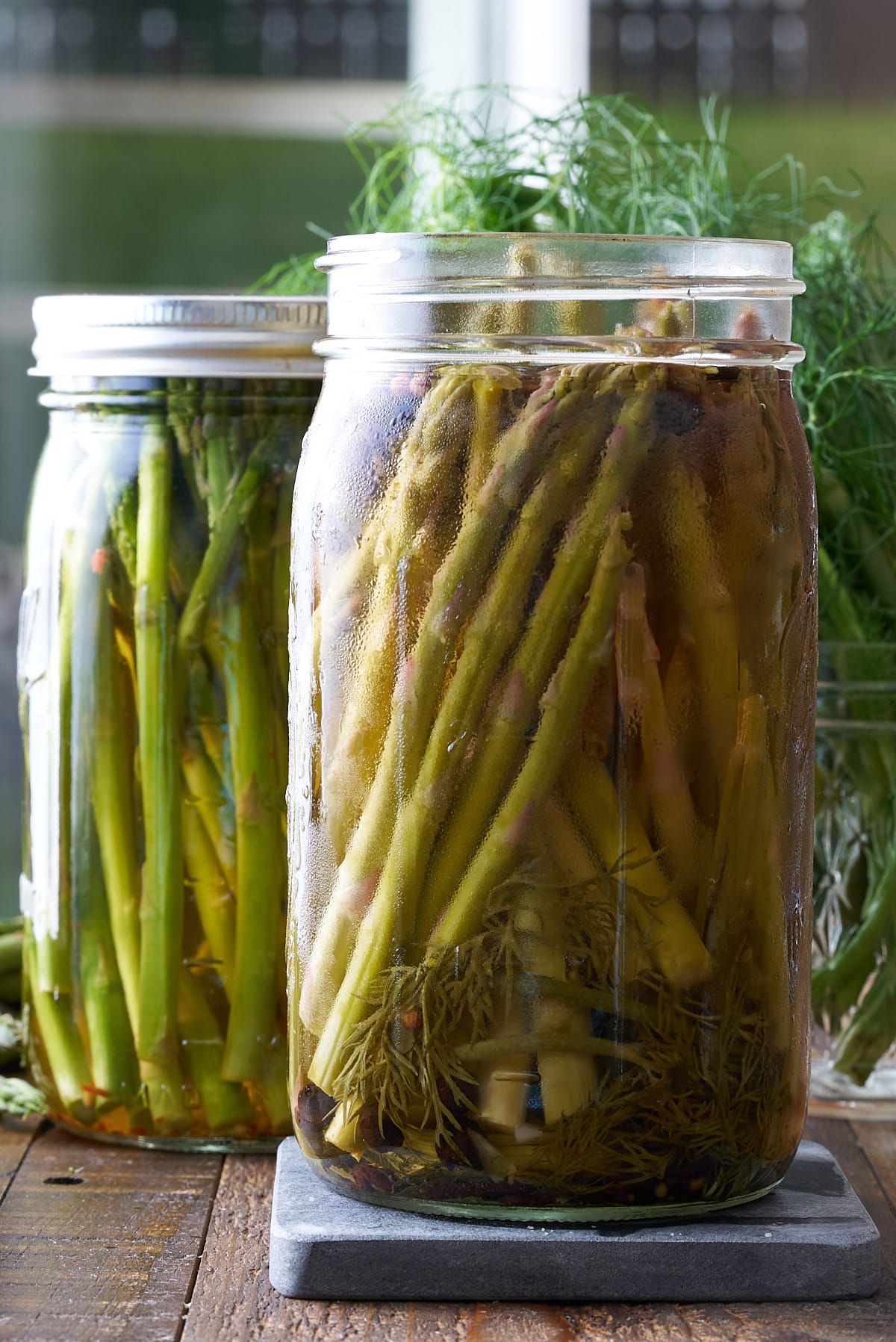 Two glass mason jars filled with pickled asparagus set onto a wooden board.