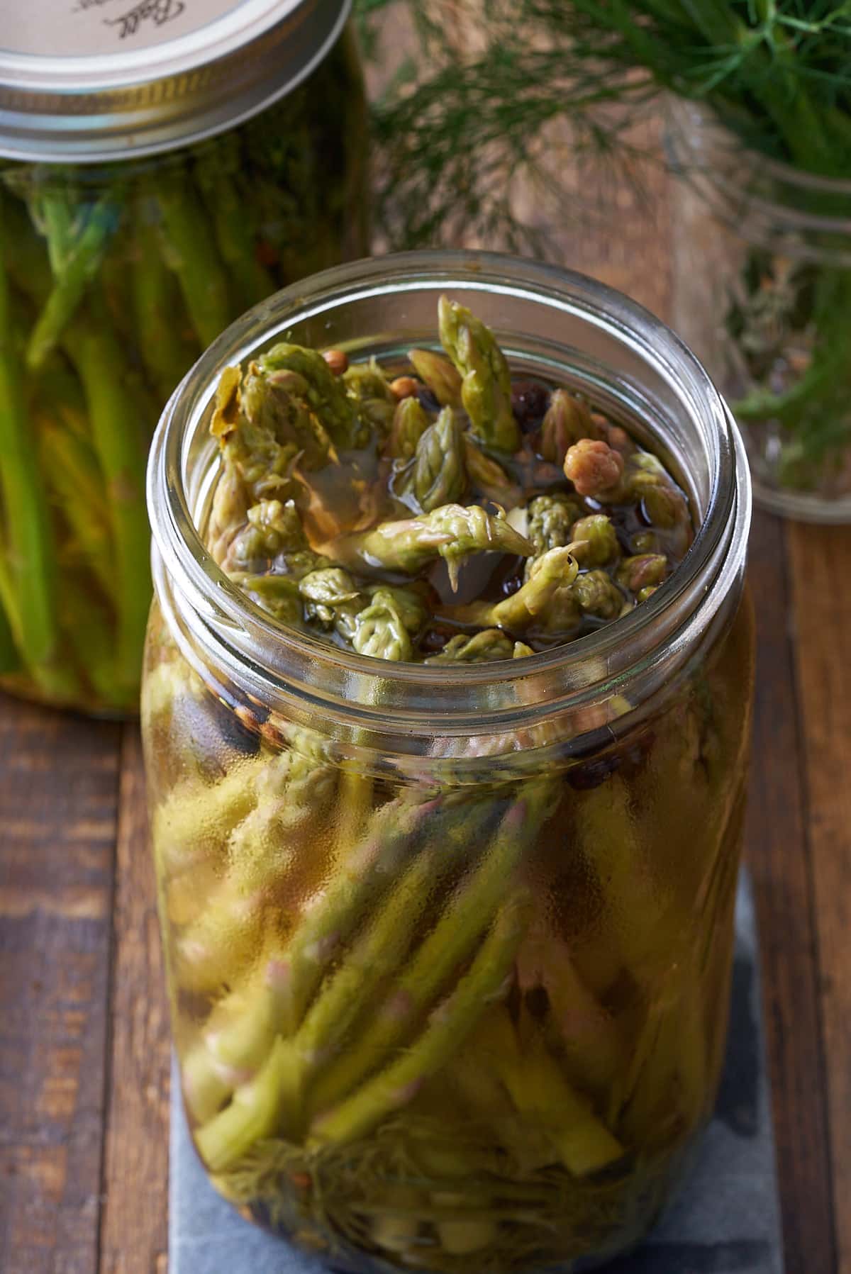 An open glass mason jar filled with pickled asparagus with another sealed jar set alongside.