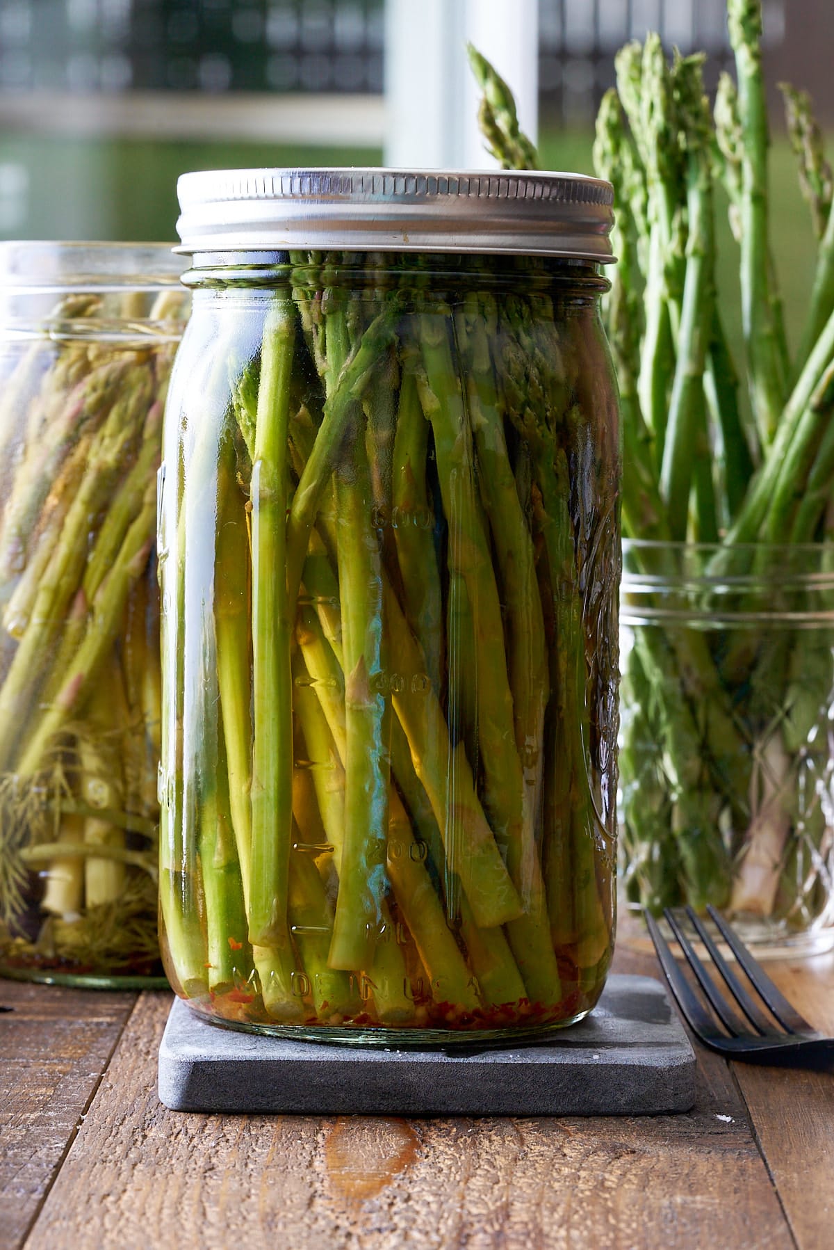 Two glass mason jars filled with pickled asparagus with a jar of fresh asparagus set alongside.