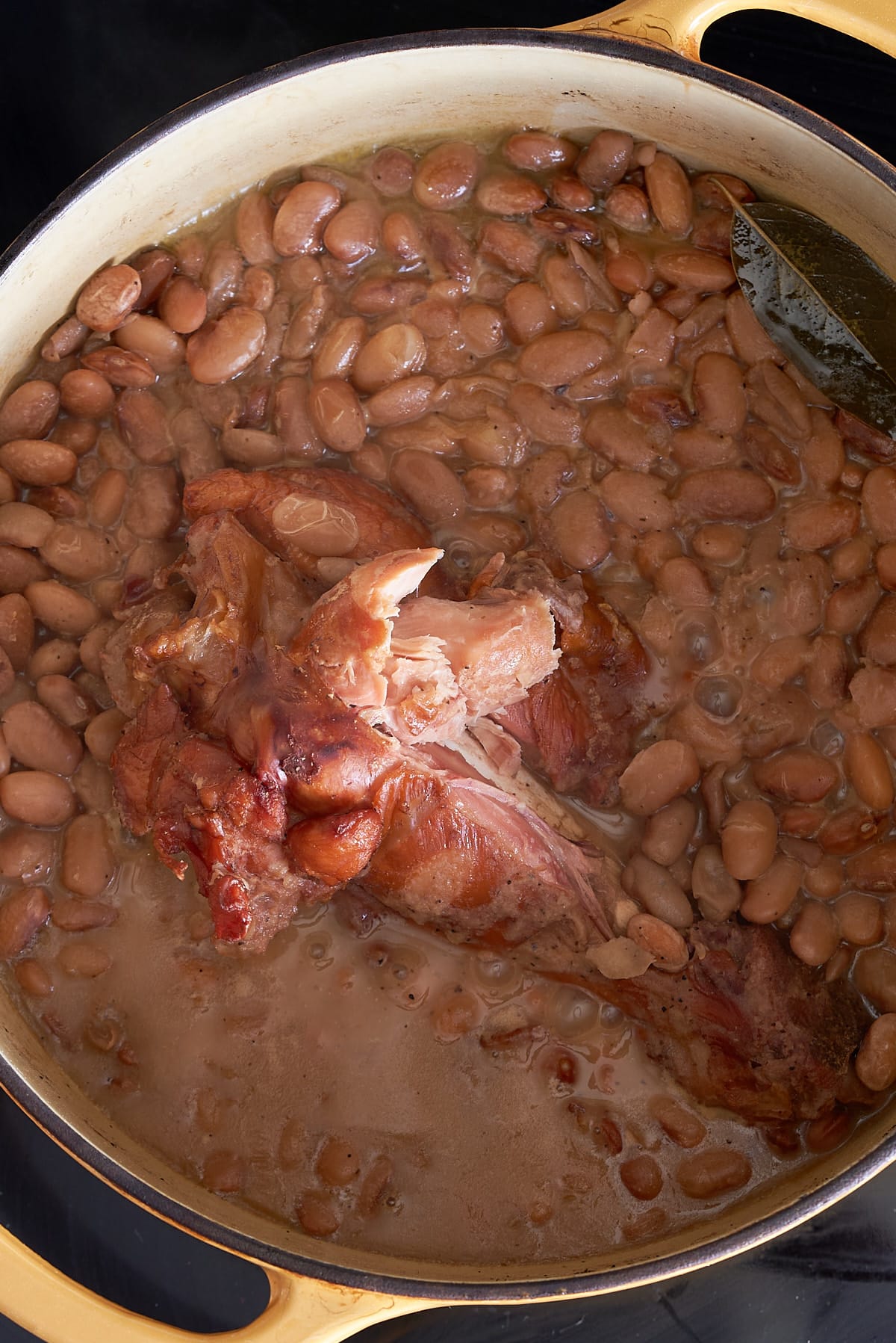 A Dutch oven filled with pinto beans and a smoked turkey leg in chicken broth.