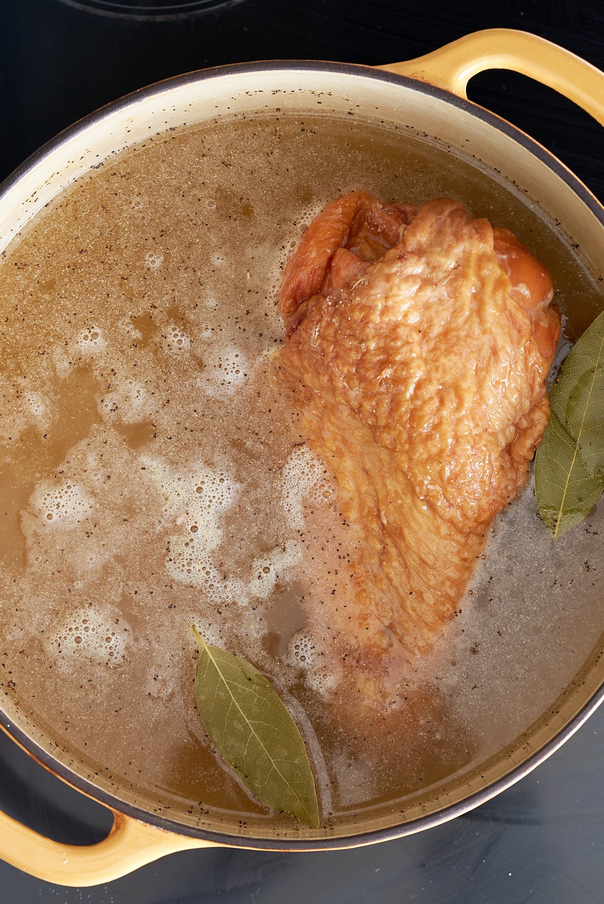 Dutch oven filled with turkey leg, chicken broth and bay leaves.