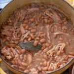 Dutch oven filled with cooked pinto beans and shredded turkey leg.