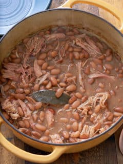 Dutch oven filled with cooked pinto beans and shredded turkey leg.
