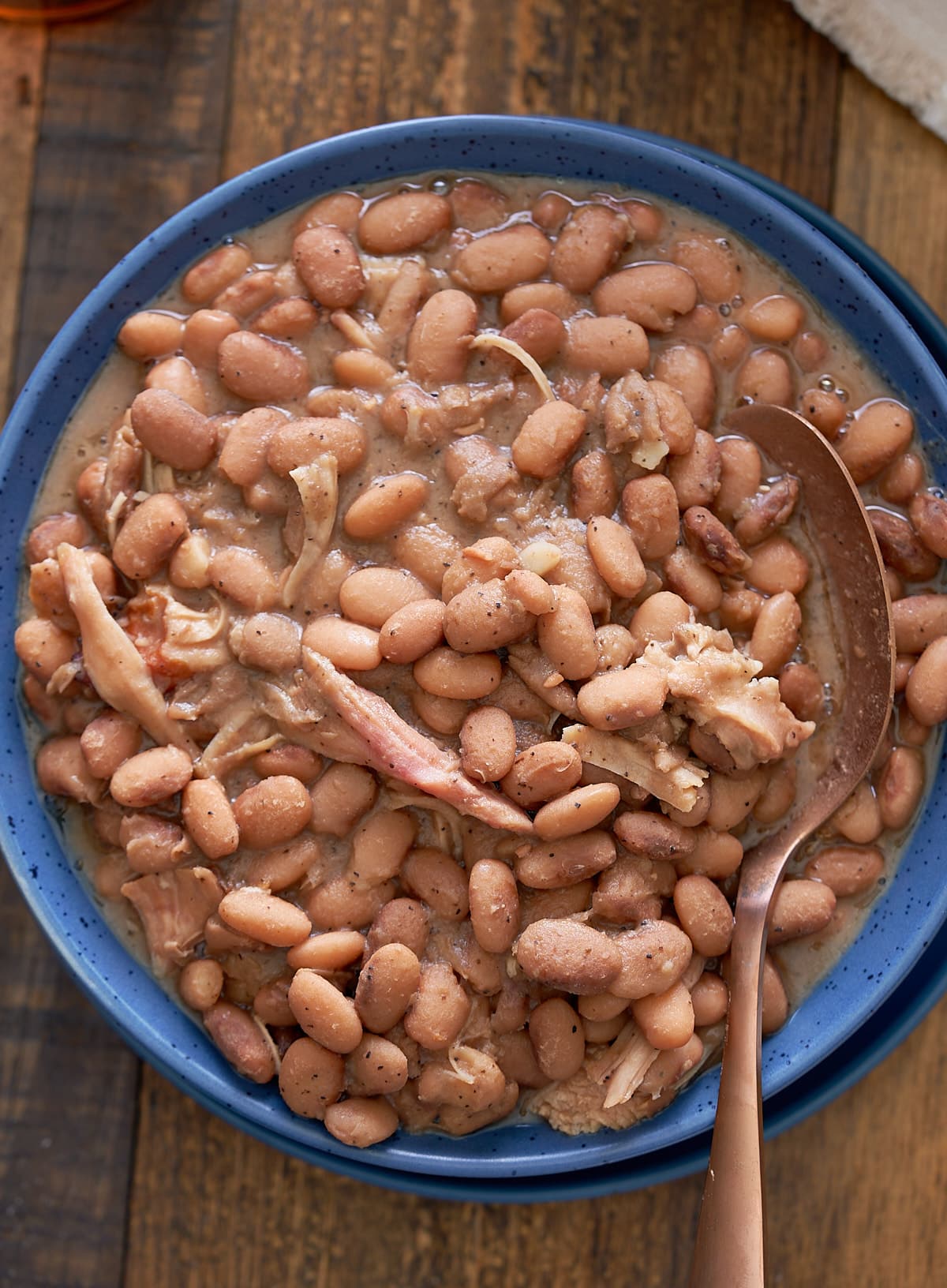 A blue bowl filled with southern style pinto beans with shredded turkey leg.