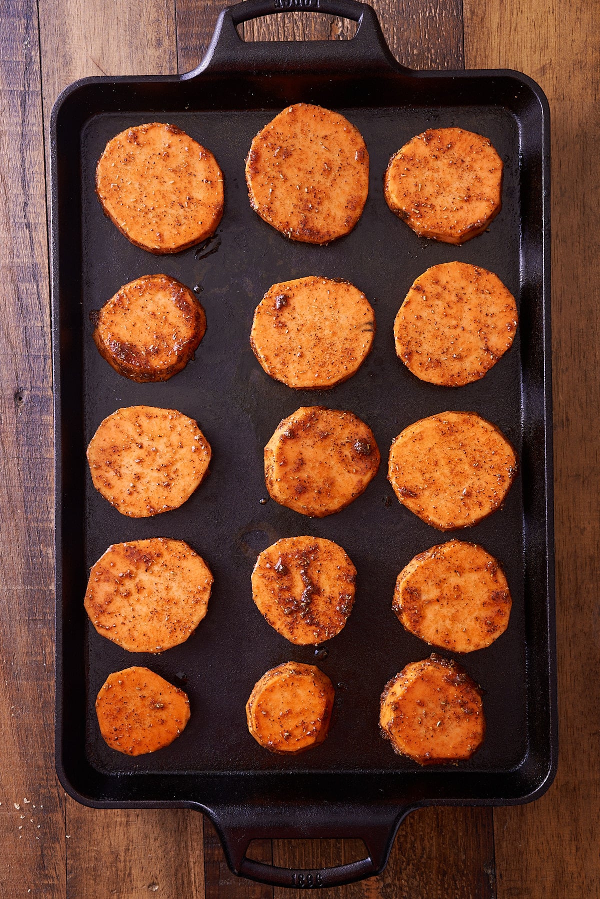 Sweet potato rounds coated in a spiced oil, set onto a prepared baking sheet ready for the oven.