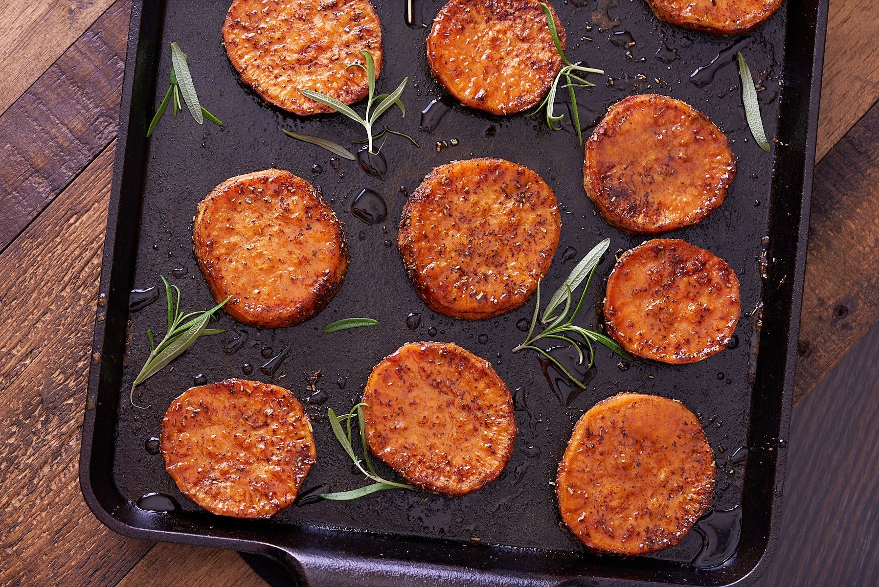 Close up image of baked sweet potato rounds on a baking sheet with springs of fresh rosemary.