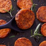Close up image of baked sweet potato rounds on a baking sheet with springs of fresh rosemary.