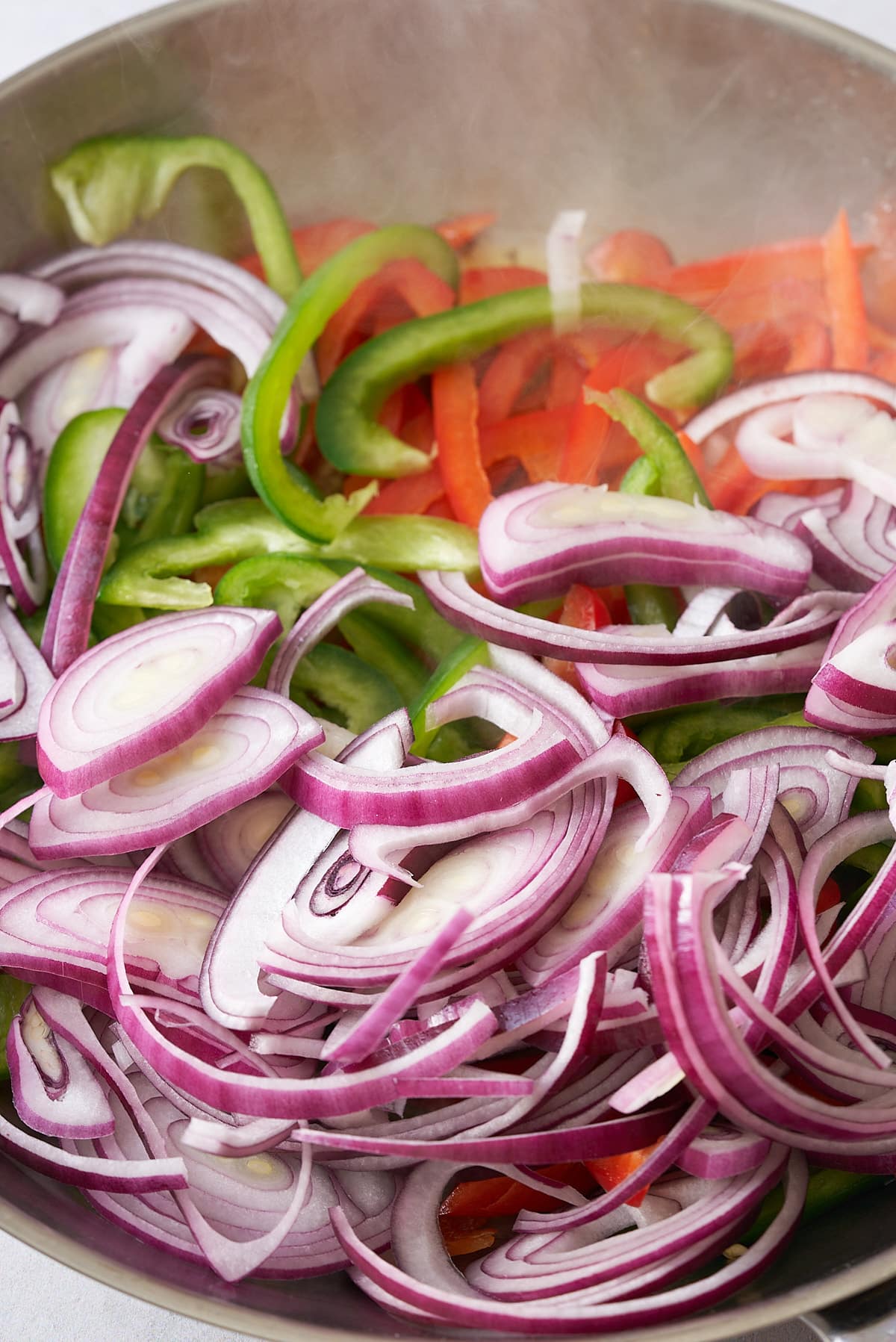 Sliced red onion and red and green bell peppers in a large frying pan.