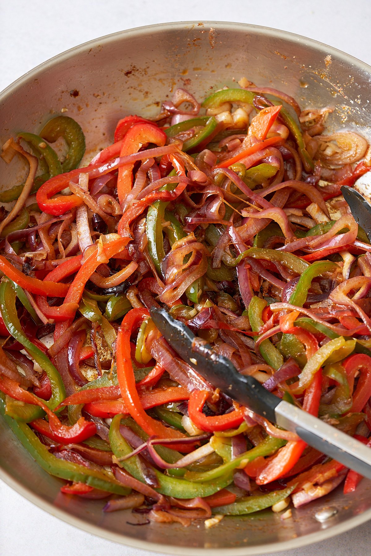 Cooked red onion and red and green bell peppers in a large frying pan.